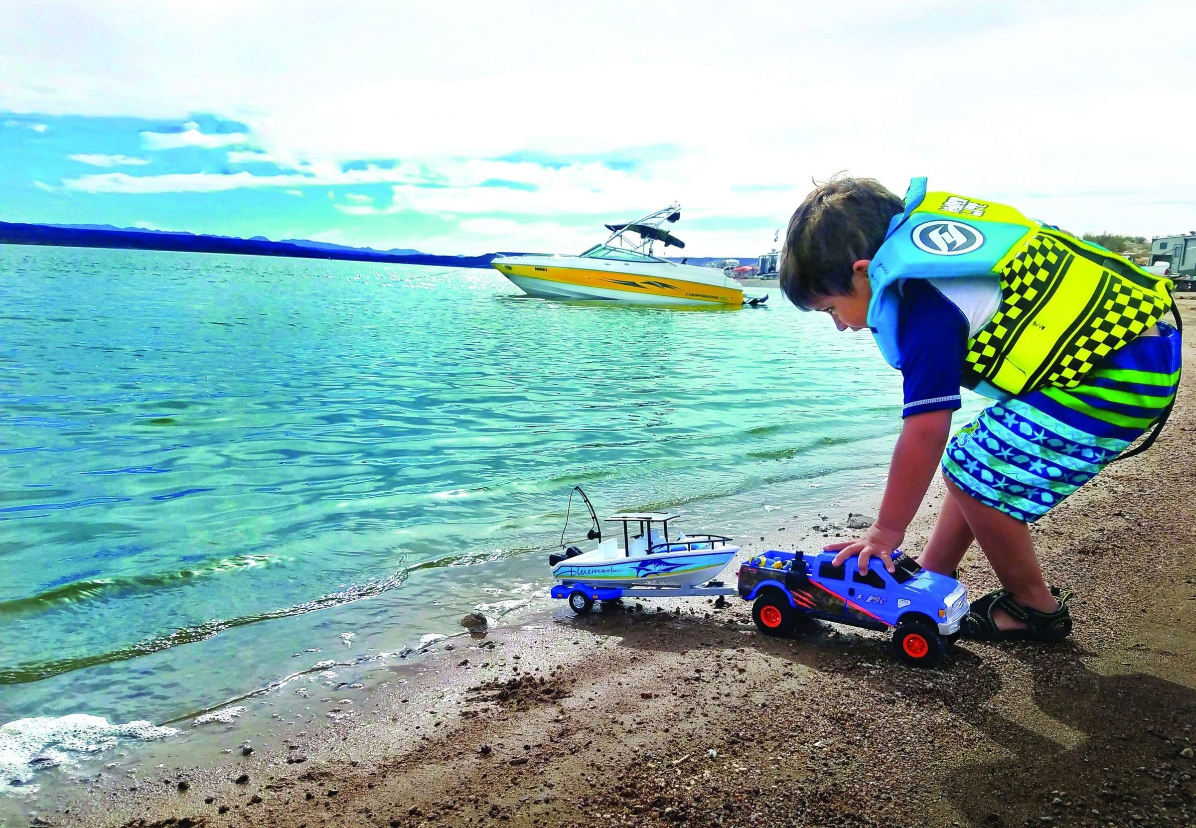 Kid playing with truck on the beach in front of a speedboat
