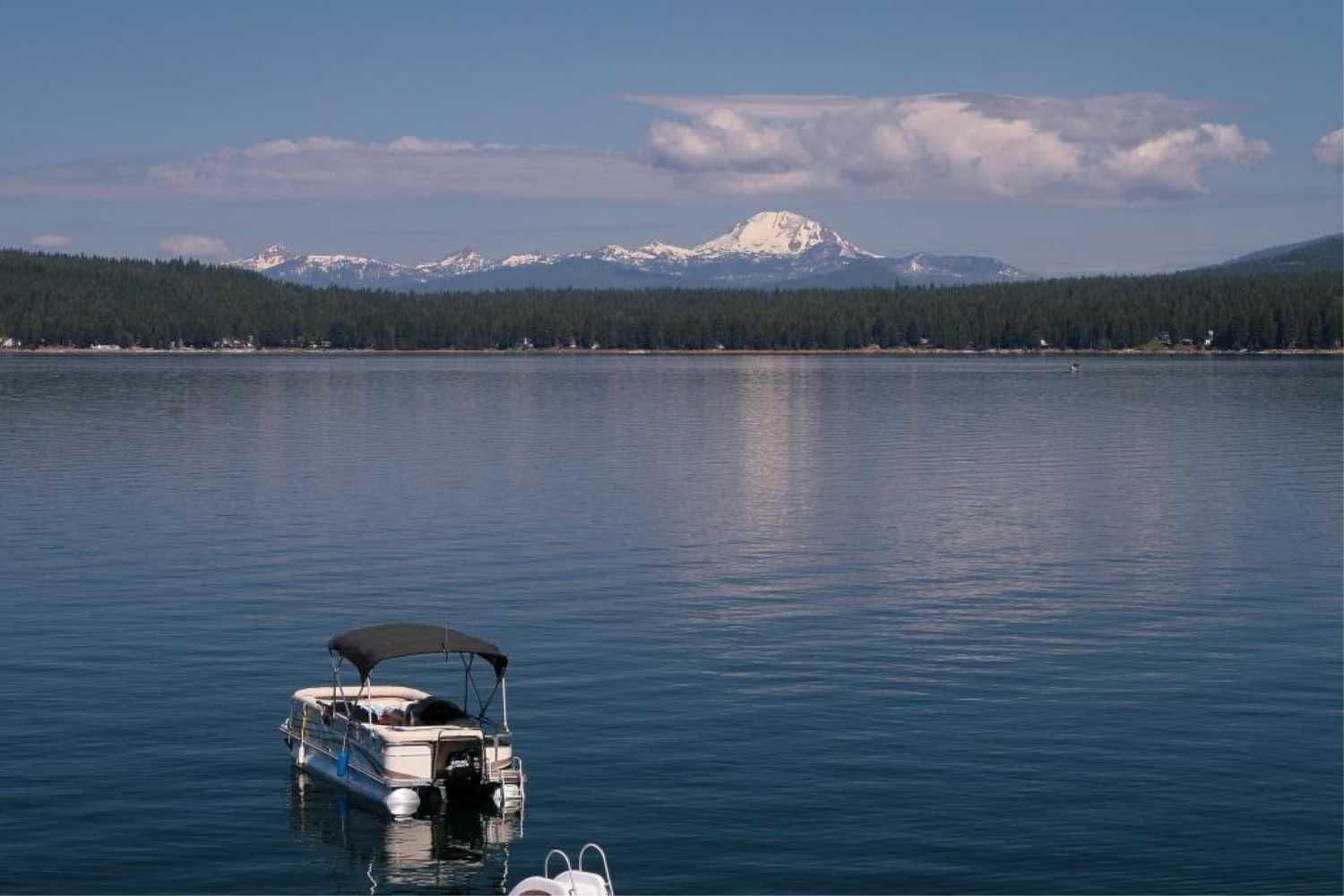 Lake Almanor with Pontoon boat on the still water with mountain range in the distance