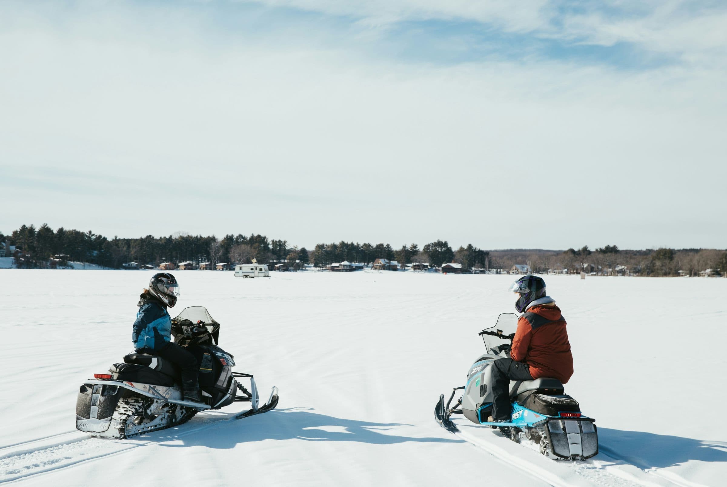Two people riding snowmobiles looking at each other