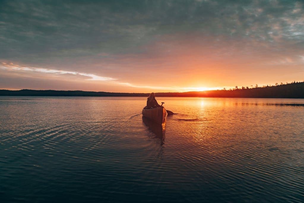 A lone canoeist paddling on Ely Lake at sunset, capturing nature's serene beauty.