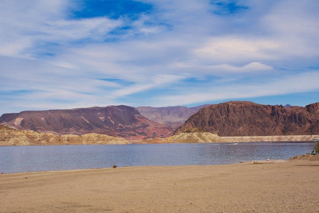 A tranquil view of a lake surrounded by rugged mountains under a clear blue sky.