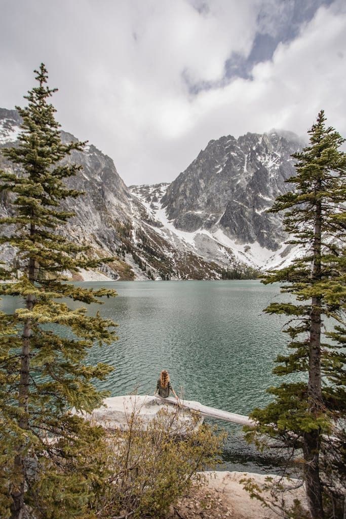 A woman admires the breathtaking mountain landscape and tranquil waters of Colchuck Lake in Washington.