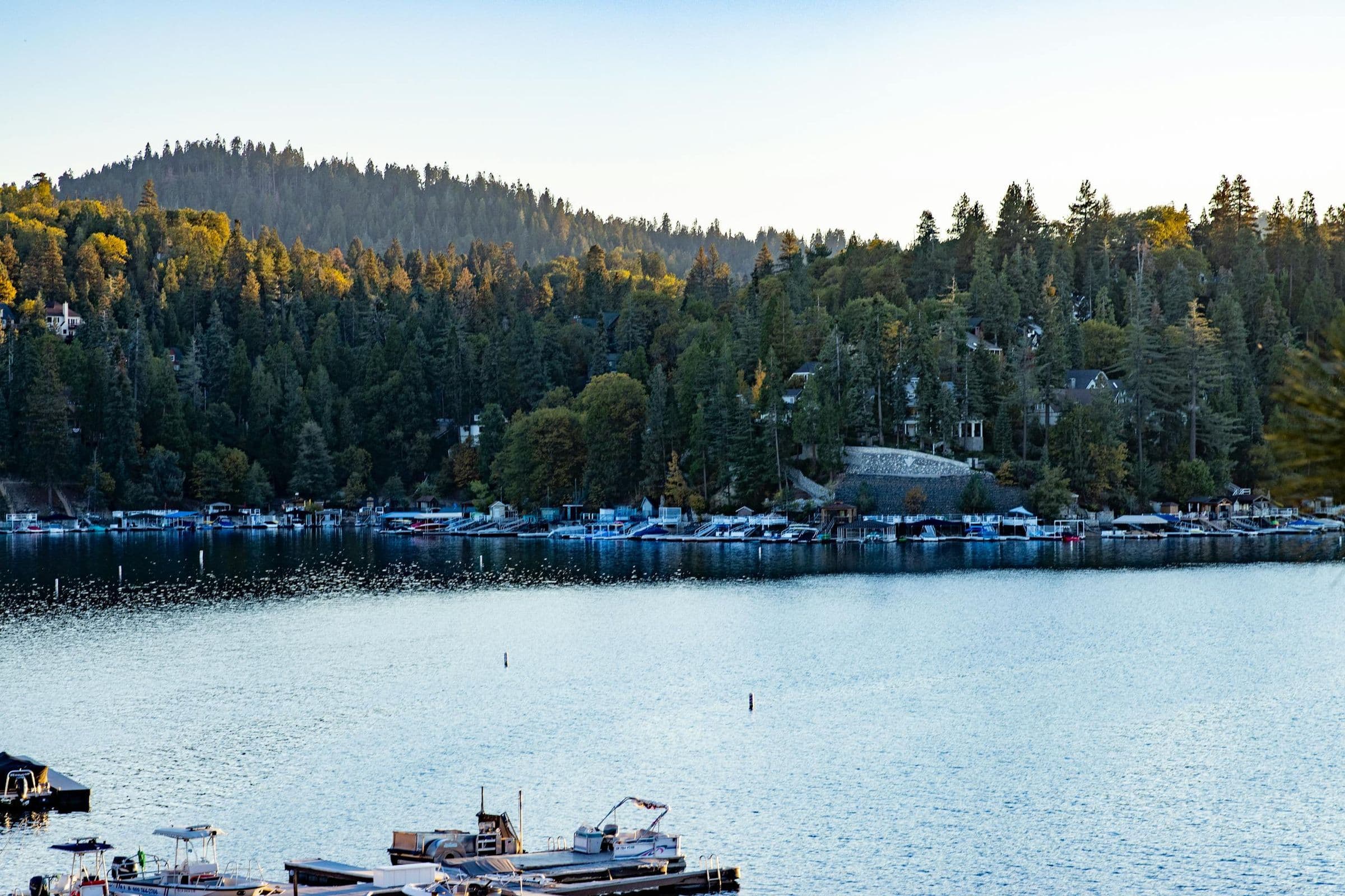 Peaceful Lake Arrowhead view with boats, surrounded by lush forest and hills.