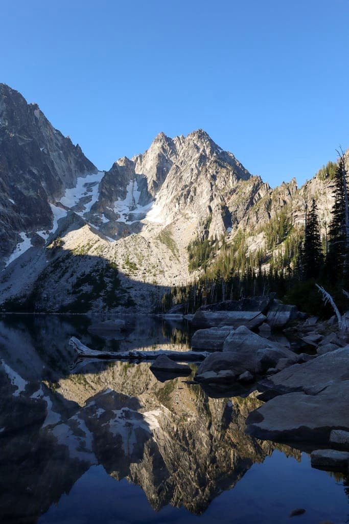 Reflective view of Colchuck Lake with the towering Cascade Mountains under a clear blue sky.
