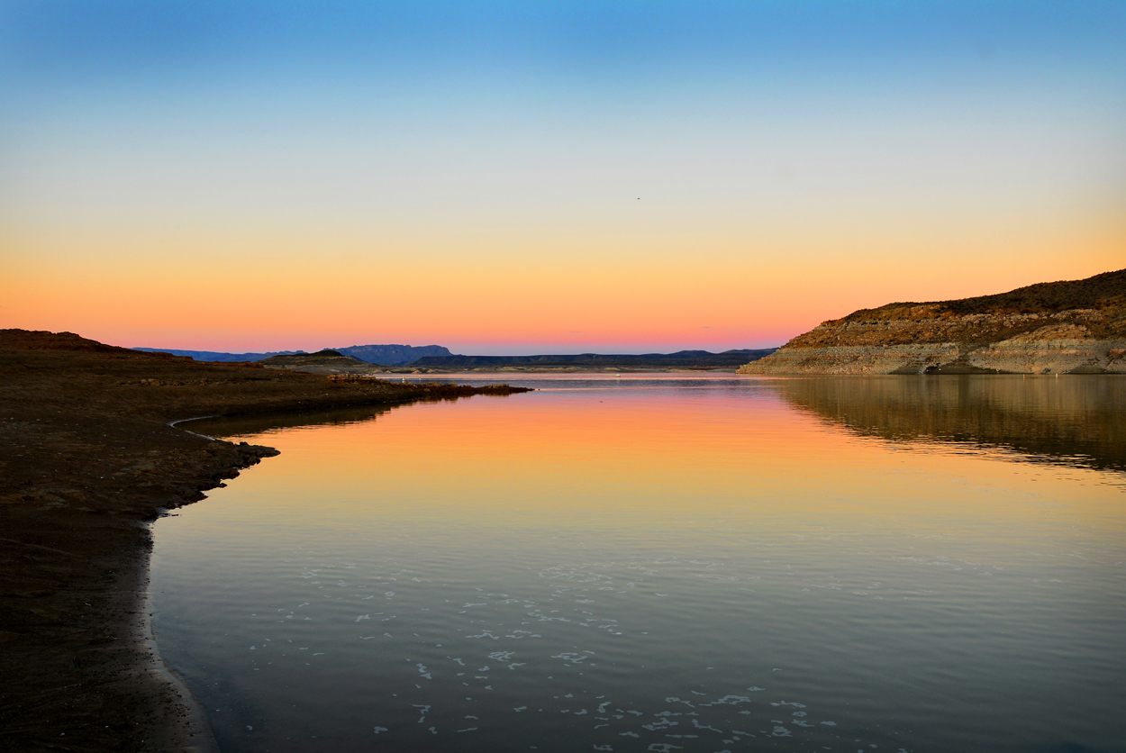 Elephant Butte Lake at sunset with vibrant colors of pinks, oranges and purples reflecting off the still waters