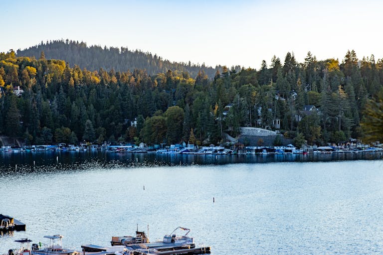 Peaceful Lake Arrowhead view with boats, surrounded by lush forest and hills.